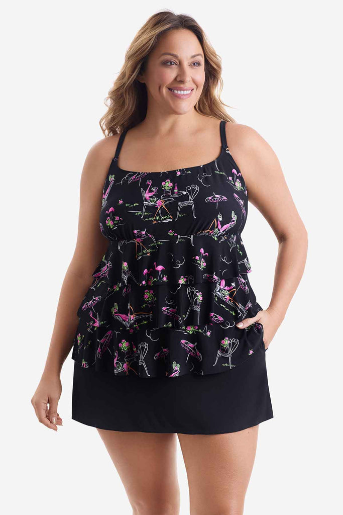 Woman wearing a black tiered one-piece swimsuit with a flamingo print with her hand in pocket