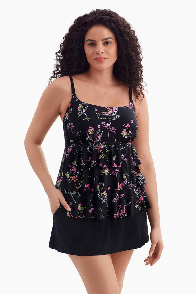 Woman wearing a black tiered swim dress with a flamingo pattern with her hand in pocket