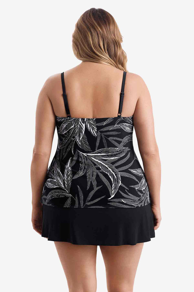 Woman turned away wearing a black tiered one-piece swimsuit with a white leaf print