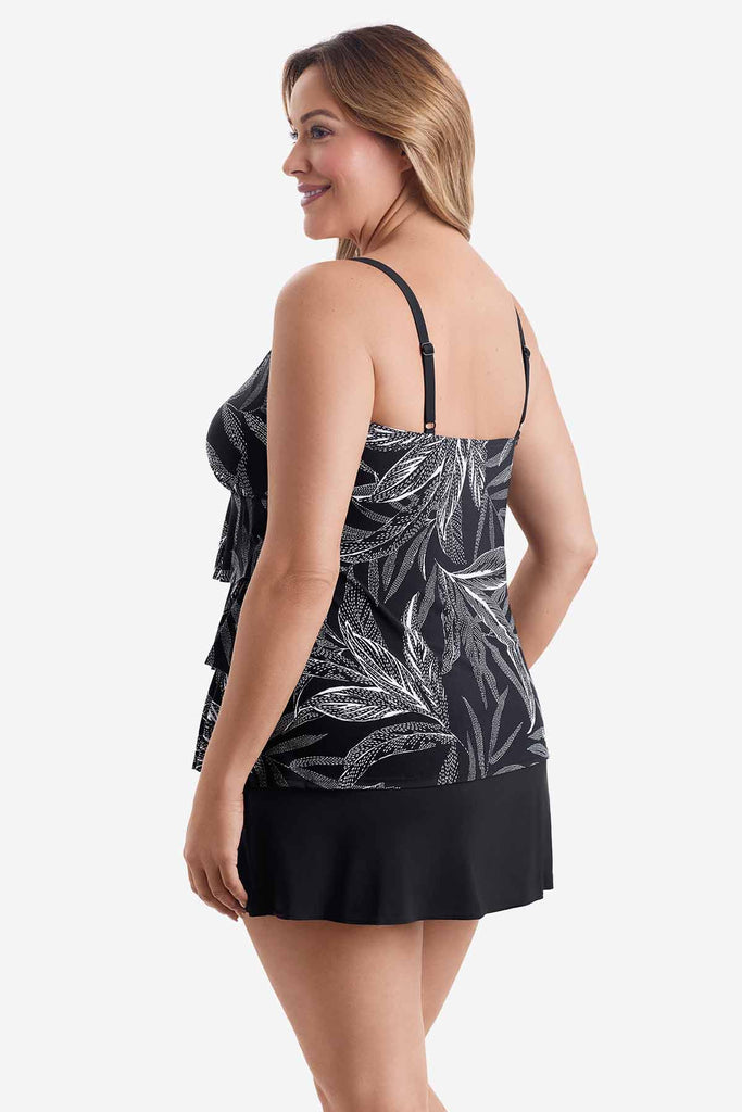 Woman turned left wearing a black tiered one-piece swimsuit with a white leaf print