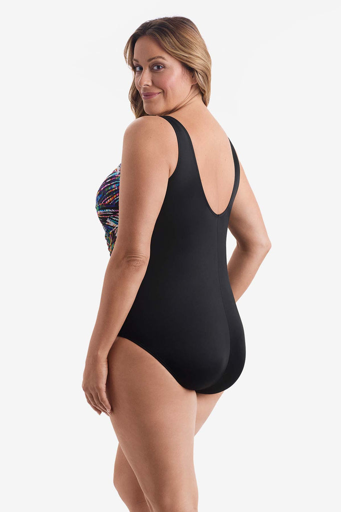 Woman turned left wearing a wrap-sash one-piece swimsuit with a multicolored pattern