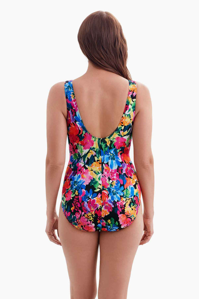 Woman turned away wearing a multicolored floral patterned one-piece swimsuit with a ruffle down the neckline 