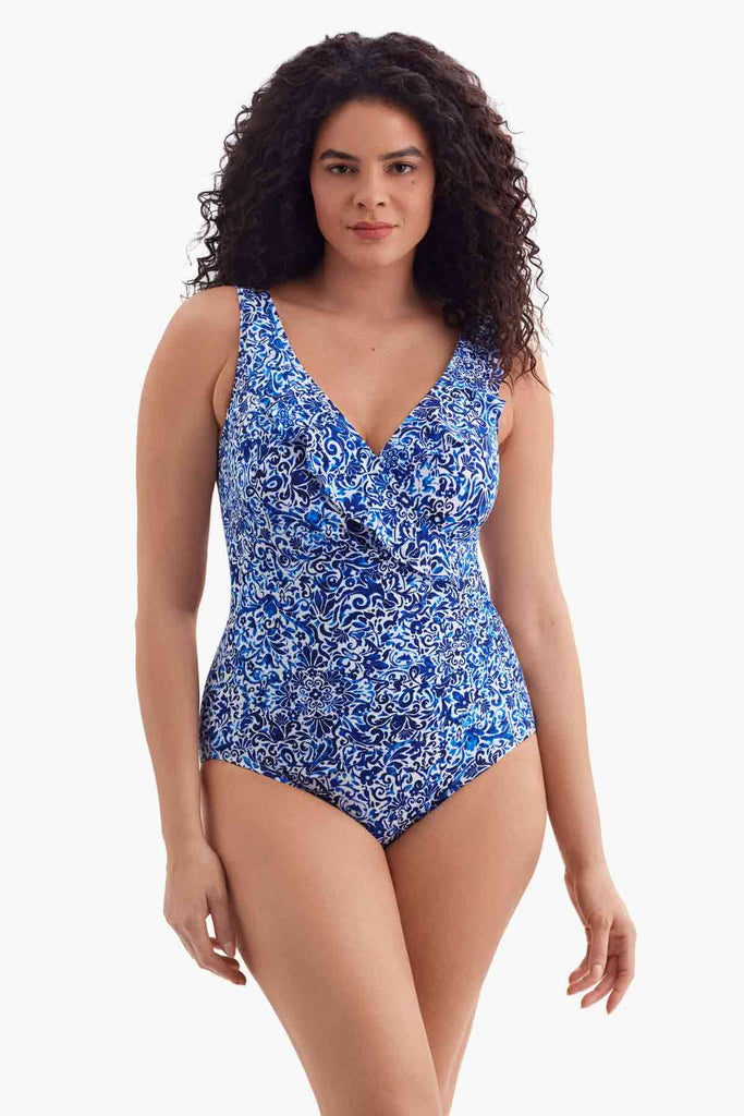 Woman wearing a blue and white abstract patterned one-piece swimsuit with a ruffle down the neckline 