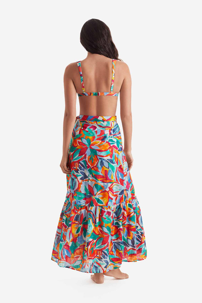 Woman turned away wearing a multicolored bikini top with a multicolored floral wrap skirt