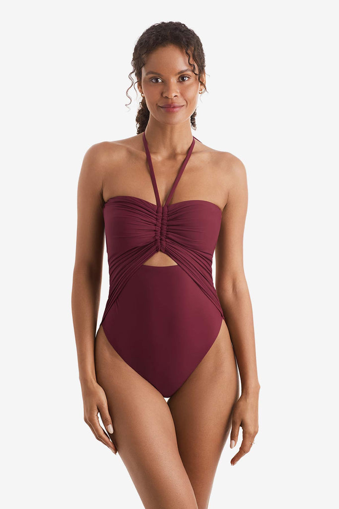 Woman wearing a dark red one-piece swimsuit with peep hole in center