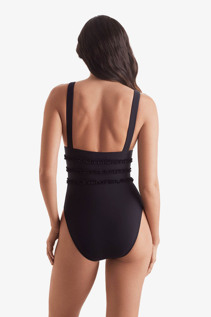 Woman turned away wearing a black one-piece swimsuit with ruffles on the waist