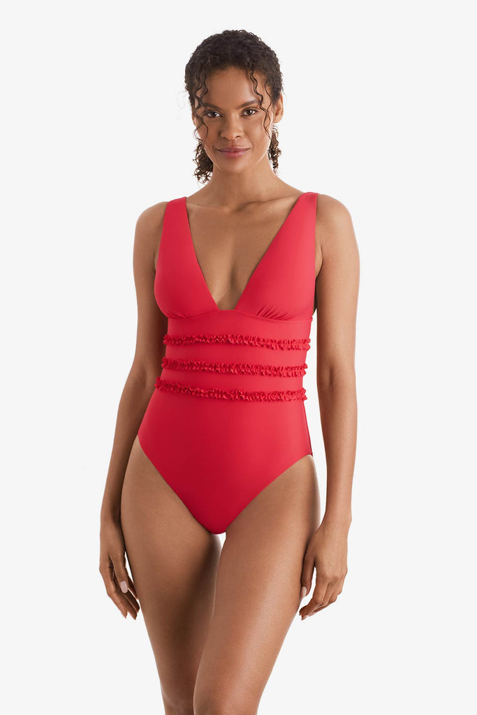 Woman wearing an orange-pink one-piece swimsuit with ruffles on the waist