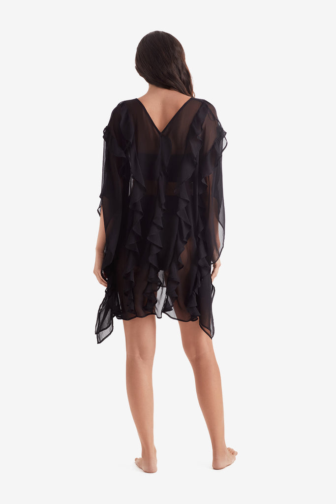 Woman faced away wearing a black sheer swim cover up with ruffles