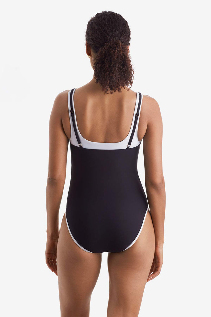 Woman turned away wearing a black one-piece swimsuit with white trim