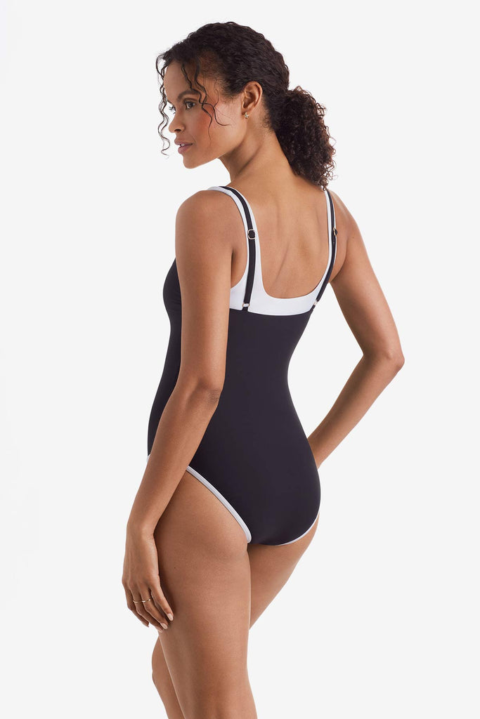 Woman turned left wearing a black one-piece swimsuit with white trim